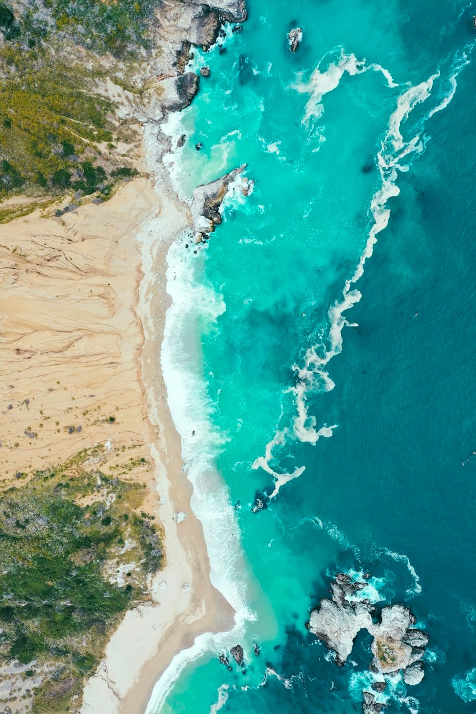 Turquoise surf breaking on a sandy shore, seen from above