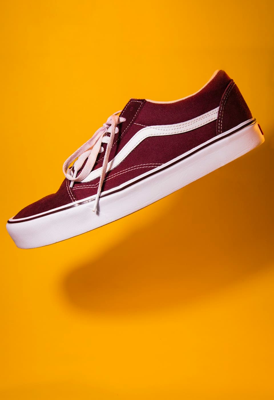 A maroon canvas sneaker on a yellow background